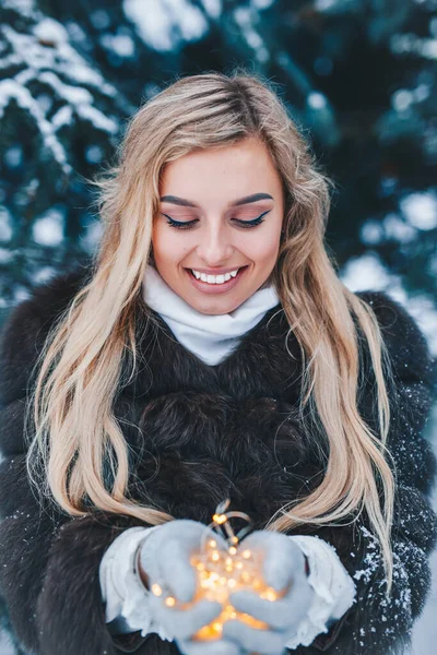 Hermosa joven holdinf luces de Navidad en sus manos en el bosque de invierno — Foto de Stock