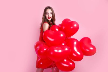 Sevgililer Günü. Pembe arka planda kalp şeklinde kırmızı balonları olan kırmızı elbiseli güzel, zarif genç bir kadın..