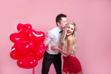 Sevgililer Günü. Pembe arka planda kalp şeklinde balonları olan mutlu genç çift..