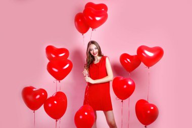 Sevgililer Günü. Pembe arka planda kalp şeklinde kırmızı balonları olan kırmızı elbiseli güzel, zarif genç bir kadın..