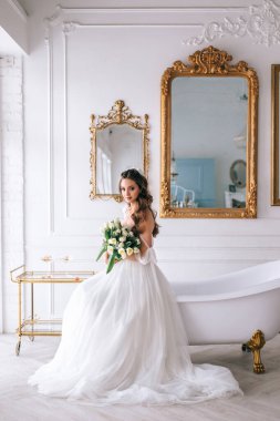 Güzel esmer gelin beyaz elbiseli, düğün buketi ile stüdyoda poz veriyor.