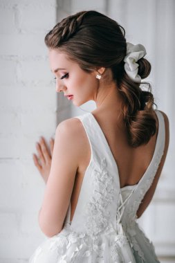 Stüdyoda beyaz bir elbise giymiş zarif sarışın gelinin arka görüntüsü.