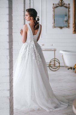 Stüdyoda beyaz bir elbise giymiş zarif sarışın gelinin arka görüntüsü.