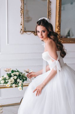 Güzel esmer gelin beyaz elbiseli, düğün buketi ile stüdyoda poz veriyor.