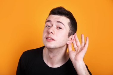 Sarı arka plandaki konuşmalara kulak misafiri olan siyah tişörtlü genç adam.