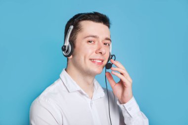 Mavi arka planda gülümseyen çağrı merkezi operatörü. Kulaklık dokunuşu.