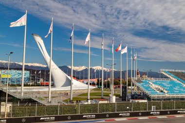 A large Olympic torch in Sochi on the background of mountains with flags of countries and stands on a sunny day.