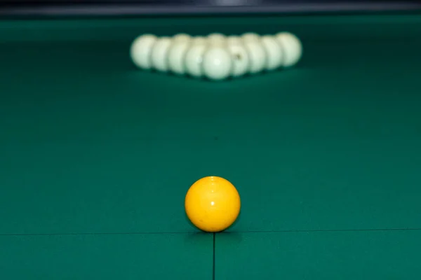 A yellow cue ball in front of a billiard pyramid on a green cloth. Russian billiards. The initial arrangement of balls in Russian billiards.