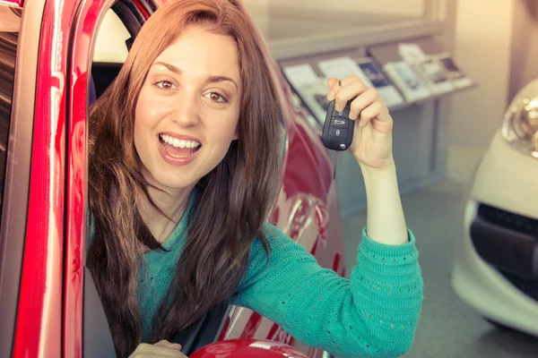 Smiling young woman holding car key inside car dealership — Stock Photo, Image