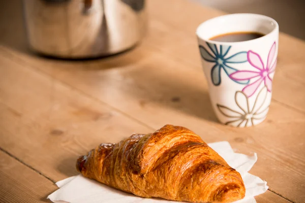 Croissant och mugg kaffe på bordet Stockbild