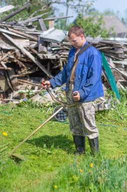 Köyde, genç bir adam çimleri bir petrol biçme makinesiyle biçiyor.. 