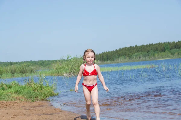 Yaz sıcağında gölün kıyısındaki kumlu sahilde oynayan bir kız..