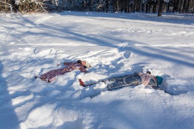 Kışın ormanda, dondurucu güneşli bir günde, bir kız karda uzanıyor ve kış eğlencesinin tadını çıkarıyor.. 