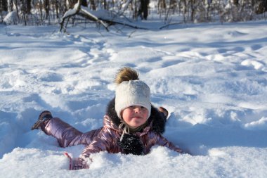 Kışın ormanda, dondurucu güneşli bir günde, bir kız karda uzanıyor ve kış eğlencesinin tadını çıkarıyor.. 