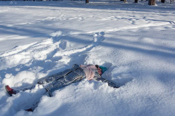 Kışın ormanda, dondurucu güneşli bir günde, bir kız karda uzanıyor ve kış eğlencesinin tadını çıkarıyor.. 