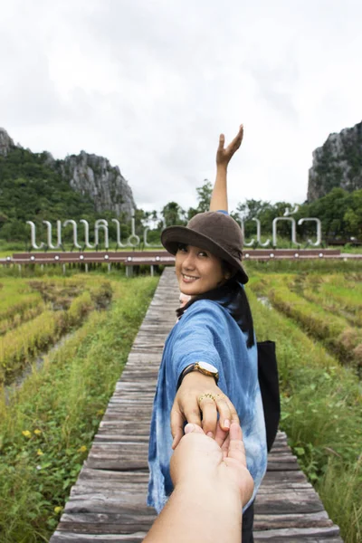 Thai woman lead man by the hand and hold on walkway wooden bridge in rice field of landmarks KaoNor KaoKaew Limestone mountains at Banphot Phisai city on October 19,2020 in Nakhon Sawan, Thailand