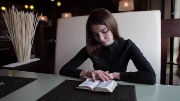 Mädchen in einem Café liest ein Buch — Stockvideo