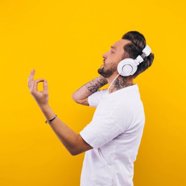 Genç adam dans ediyor ve müzik dinliyor. Duygular, yüz ifadeleri, duygular, vücut dili, işaretler. Sarı bir stüdyo arkaplanındaki görüntü.