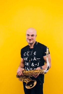 Stüdyoda sarı arka planda saksafon tutan bir adam.