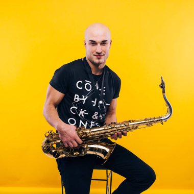 Stüdyoda sarı arka planda saksafon tutan bir adam.