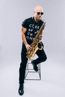 Adam stüdyoda gri bir arkaplanda saksafon çalıyor.