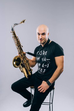 Elinde saksafon olan bir adam, stüdyoda gri arka planda.