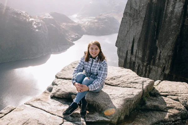 ノルウェーのプリケストロール山 Pulpit Rock の上に可愛い女の子が座っています ストック画像