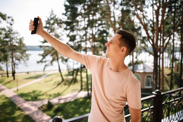 若い男がバルコニーに立ち 自分の携帯電話で自撮り ストック写真