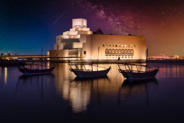 Doha Katar 'daki İslami Sanatlar Müzesi. Gece çekimleri. Aydınlatılmış müzenin eşsiz mimarisini ön planda Arap körfezinde eşarplarla gösteriyor.