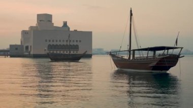 Doha Katar 'daki İslam Sanatları Müzesi' nin dış gün batımı çekimleri Arap Körfezi 'nde ön planda Katar bayrağı ve arka planda bulutları gösteren görüntüler.