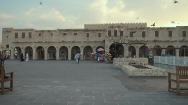 Souq Waqif, Doha Katar 'ın ana caddesinde alacakaranlıkta, yerli halk ve ziyaretçilerle zumluyor eski çeşme ve güvercinler uçuşuyor.