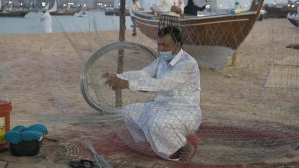 在卡塔尔多哈举行的卡塔拉第十个传统三角帆船节上 一名阿拉伯手工艺者坐在海滩上 在下午把鱼网放大 — 图库视频影像
