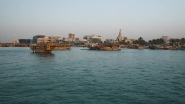 Doha ufuk çizgisi Corniche gezinti alanından gün batımına doğru yaklaşıyor ve çekimde ön planda Katar bayrağıyla eşleşmeleri gösteriyor. 