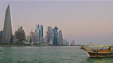 Doha, Katar-26 Ekim 2025: Katar bayrağıyla Arap körfezinde dhows 'u gösteren Corniche gezinti günbatımından Doha Katar silueti