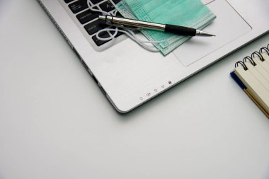 Beyaz arkaplanda defter, kalem, tıbbi maske ve defter