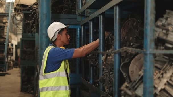 身穿安全制服 手套和头盔的年轻亚洲男性工人检查库存 如发动机 机械零配件和其他堆放在汽车工业工厂仓库货架上的物品 — 图库视频影像