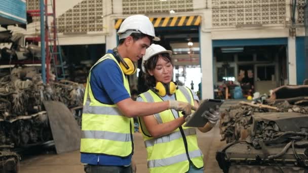 亚洲男女工人穿着制服和钢盔 对汽车配件仓库工厂的员工进行库存检查 使用平板电脑检查汽车行业的旧引擎和机器订单 — 图库视频影像