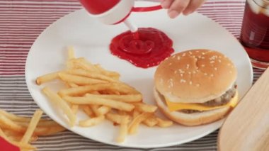 Yakın çekimler, abur cuburlar için kırmızı şişelerden dökülen masa örtüleri üzerine ketçapa odaklanmış hamburgerler, patates kızartmaları, abur cuburlar ve kola.. 