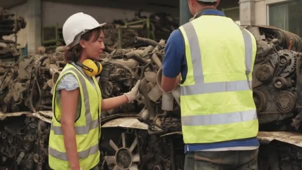 亚洲男女工人穿着制服和钢盔 对汽车配件仓库工厂的员工进行库存检查 他们谈论汽车工业的旧发动机和机器技术 — 图库视频影像