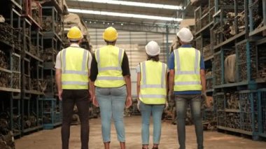 Fabrika güvenliği üniformalı çeşitli ırkların çalışanları sevinçlerini ifade ediyorlar. Geri dönerek, otomotiv endüstrisi için motor parçaları ve makinelerden oluşan bir depoda kollarını kavuşturdular..