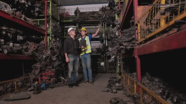 白人业主和亚裔工人 两个人在仓库里检查发动机零件 他们两个人都在工作时戴着钢盔 所以大部分产品都是汽车行业的机器 — 图库视频影像