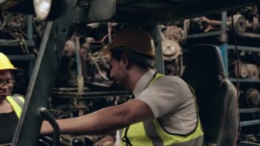 Beyaz erkek forklift sürücüsü, endüstriyel fabrikaların depolarındaki motor ve makine parçalarını kontrol etmek için siyah bir kadın mühendisi bekliyor. Ve kız geldiğinde, adam geri geri gitti..