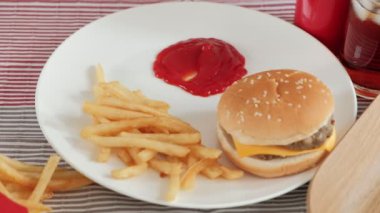 Yakın çekim, seçici odak: Adamın eli kızarmış patates yiyordu, kırmızı masa örtüsünde kırmızı bir masa örtüsüne ketçap ve hamburger ve kola batırıyordu. Öğle yemeği için abur cubur ya da fast food yemek sağlıksız..