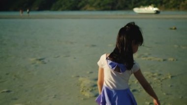 Uzun siyah saçlı, mor mayo giymiş ve çıplak ayaklı Asyalı bir kız yaz tatilinde plajda oynuyor. Gün batımında güzel bir adada ıslak kumun üzerine yazıp çizerek..