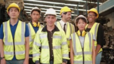 Bulanık odak noktası VDO: Üniformalı ve miğferli bir grup mühendis kollarını kavuşturup mutlu bir şekilde gülüyor. Tüm iş arkadaşları makine yedek parça depolama fabrikasında profesyonel takım çalışmasıdır..