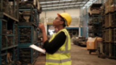 Bulanık odaklı VDO: Güvenlik formundaki siyah kadın işçiler ve kasklar bir fabrikanın deposundaki yedek motor parçalarını kontrol ediyor. Ve neşeli beyaz erkek mühendis meslektaşı tarafından karşılandı..