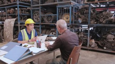 Otomobil deposunda iki adam var: Kafkas müşterisi ve Asyalı erkek motor parçaları satıcısı fabrikada iş anlaşması için pazarlık ediyorlar. Makinelerin istiflendiği masada konuşarak..