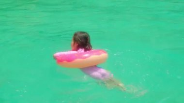 Islak mayo ve pembe şamandıralı şirin Asyalı turist kız yüzüyor. Ve zümrüt mavisi denizde suyla oynayarak rahat, keyifli ve mutlu bir yaz tatilinde.