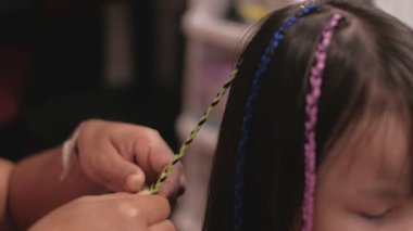Yakın plan VDO: Güzel, uzun siyah saçlı Asyalı kız güzellik salonunda çok renkli ipliklerle örülüyor. Çocuk modası, örgü ören örgü ören örgü ören yün örgüler..