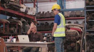 Otomotiv deposundaki iki adam: Kafkas sahibi siparişleri kontrol etmek için dizüstü bilgisayar kullanıyor ve fabrikadaki endüstriyel motor parçaları yüzünden Asyalı bir erkek çalışanı suçluyor..